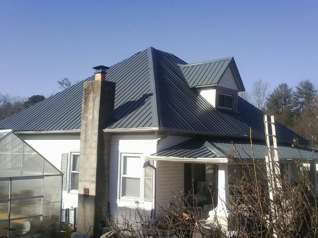 Dark blue standing seam metal roof on a white farmhouse with dormer — Slate & Tile Roof Repair by Roofing Brothers in Levasy