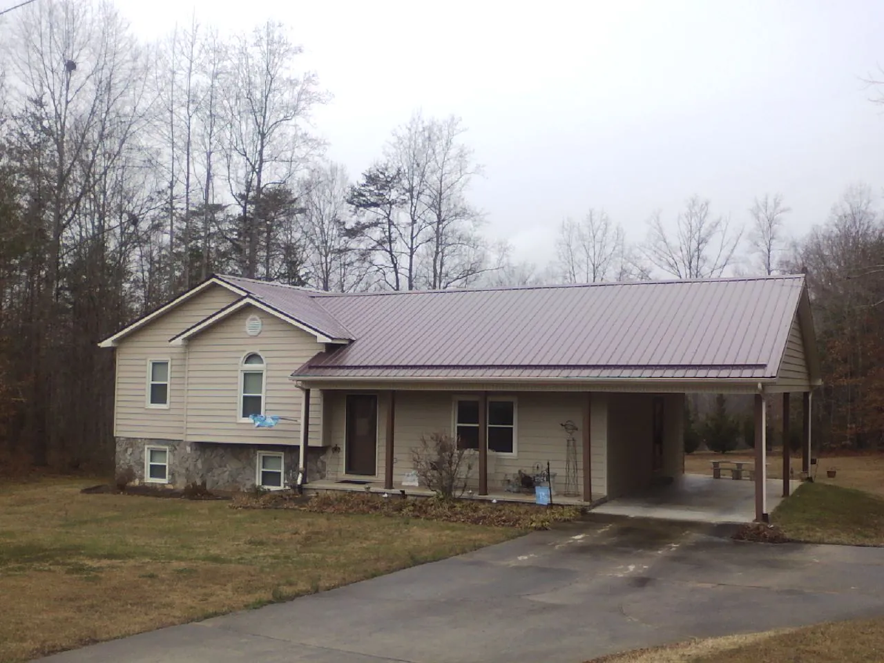 Burgundy metal roof on a tan split level home with an attached carport in Levasy