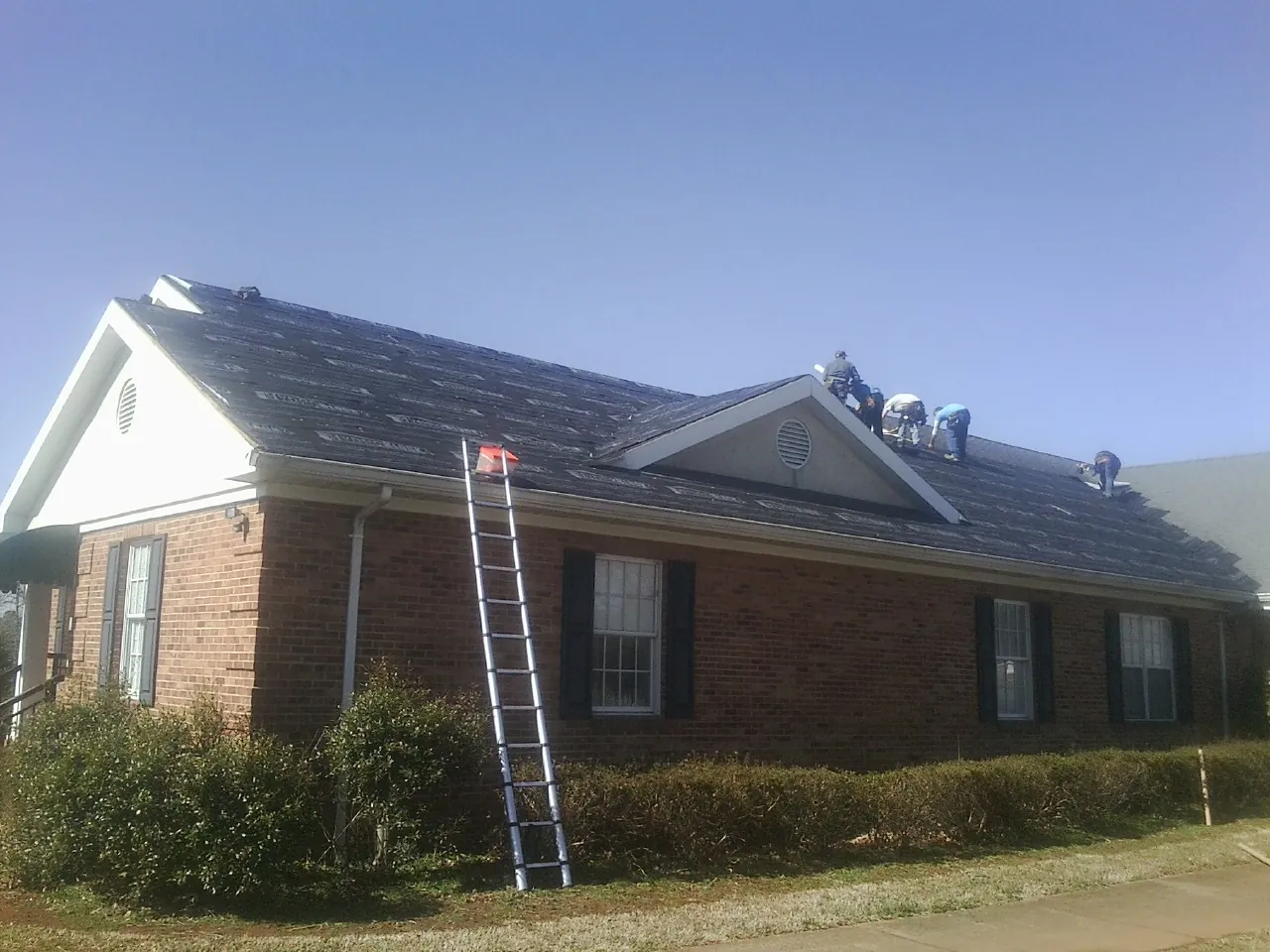 Crew tearing shingles off a brick ranch roof with a ladder set — Emergency Roof Repair work by our crew in Levasy