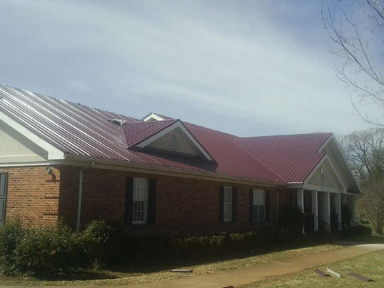 Red metal roof with gabled entries on a long brick building, from a Hail Damage Roof Repair job in Levasy