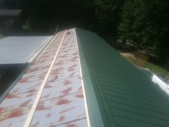 Old rusted panels beside newly installed green metal roofing — Wind Damage Roof Repair by Roofing Brothers in Levasy