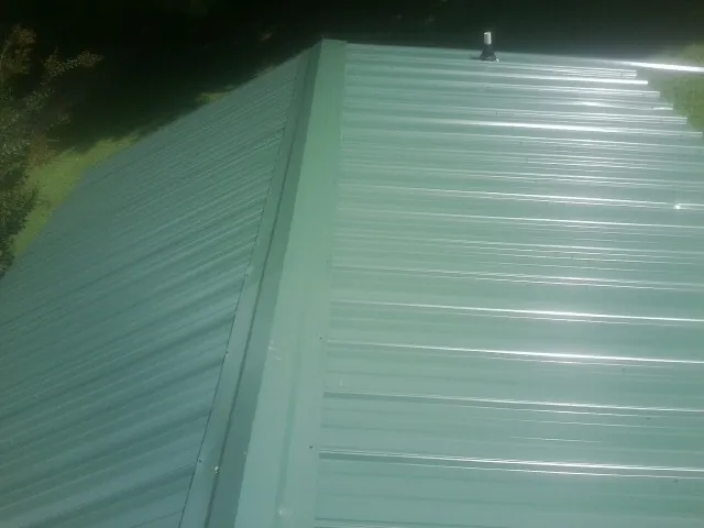 New green metal panels meeting at the ridge of a roof — Flat Roof Repair work by our crew in Levasy
