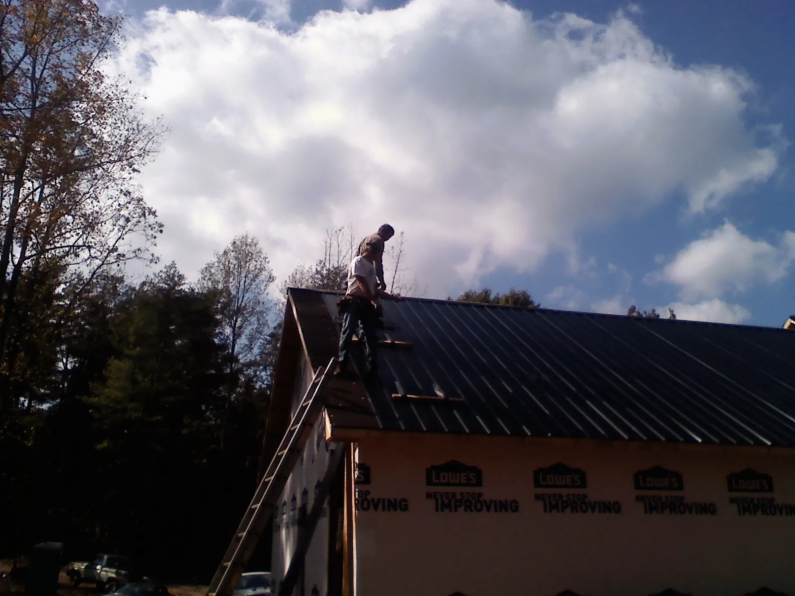 Roofer fastening dark metal panels high against a cloudy sky, from a Roof Inspection job in Levasy