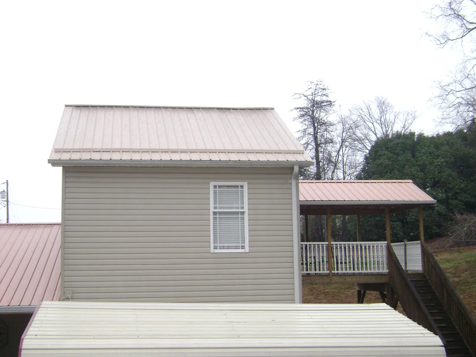 Tan metal roofs on a two story addition and attached porch, from a Roof Replacement job in Levasy